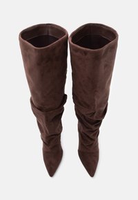 Brūnas zamšādas zābaki virs ceļa ar izteiktu krokotu dizainu, smailu purngalu un apvītām aprocēm. Mīksta tekstūra ar bagātu, dziļu krāsu.