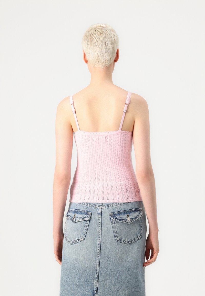 Różowa dzianinowa bluzka bez rękawów o prążkowanej strukturze, z regulowanymi ramiączkami i falbaniastymi krawędziami, zestawiona z niebieską spódnicą dżinsową z tylnymi kieszeniami.