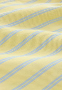 Žltá látka s rovnomerne rozmiestnenými diagonálnymi svetlomodrými pruhmi, ukazujúca mäkký, textúrovaný povrch s jemnými záhybmi.