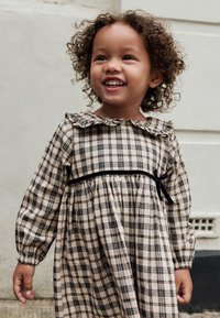 Beige and black plaid dress with long sleeves, a ruffled collar, and a black ribbon tie at the waist. Smooth fabric with a slight sheen.