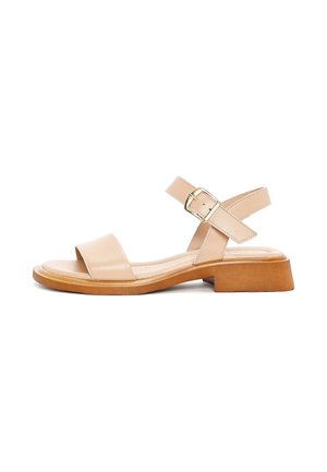 Sandal in pelle beige con punta aperta e due cinturini incrociati. Presenta una chiusura con fibbia e una suola spessa di colore marrone chiaro.