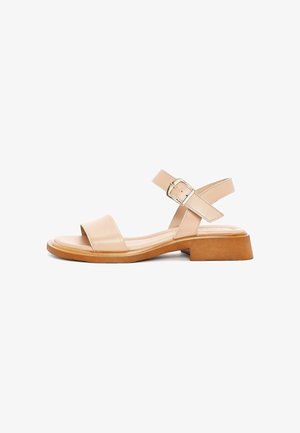 Beige leren sandaal met een open teen en twee kruisbanden. Kenmerkt zich door een gespsluiting en een chunky, lichtbruine zool.