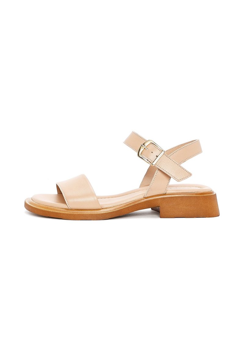 Sandal in pelle beige con punta aperta e due cinturini incrociati. Presenta una chiusura con fibbia e una suola spessa di colore marrone chiaro.