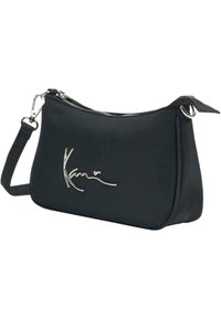 Sac à bandoulière noir avec une fermeture éclair argentée et une bandoulière chaîne, avec un logo argenté en cursive sur le devant.