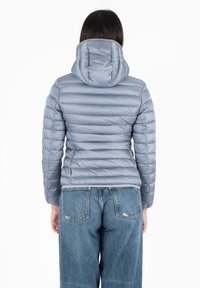 Giubbotto piumino grigio chiaro con motivo trapuntato orizzontale e cappuccio. Presenta polsini elasticizzati e una texture liscia e lucida. Abbinato a jeans blu.