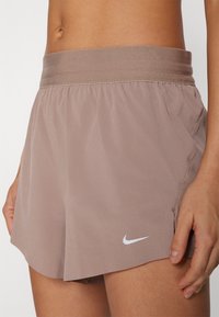 Nike hardloop shorts in lichtbruin, gemaakt van lichte stof. Voorzien van een elastische tailleband en een klein wit logo aan de zijkant.