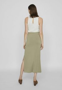 Top de tirantes acanalado verde claro con detalle de abertura en la espalda, combinado con una falda larga y fluida que presenta una abertura lateral. Zapatos de tacón grueso marrones.