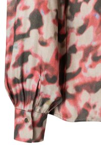 Blouse à manches longues avec un imprimé abstrait rose, noir et crème, présentant des manches froncées et un détail de poignet à bouton.