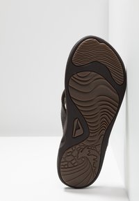 Suola di sandalo marrone con un motivo testurizzato caratterizzato da scanalature e linee ondulate, realizzata in gomma resistente con accenti triangolari.
