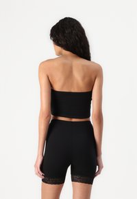 Svart stroppeløs crop-top kombinert med high-waisted shortser med blonder i kanten. Glatt, elastisk stoff med tettsittende passform.