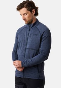 Marineblauwe zip-up jas met een gestructureerd patroon, beschikt over een hoge kraag en een borstzak, gedragen met donkere broek.
