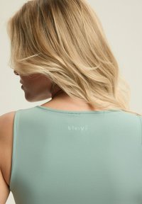 Jasnozielony top bez rękawów o gładkiej fakturze i okrągłym dekolcie. Posiada subtelne logo ("blovii") na plecach.