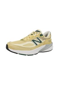 Zapatilla deportiva amarilla y gris con parte superior de malla y ante, acentos verdes, suela acolchada y dibujo texturizado en la suela exterior.