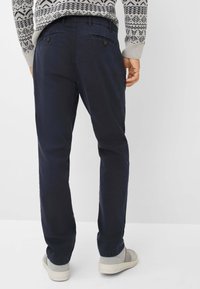 Marineblauwe broek van een katoenmix met een rechte pasvorm en achterzakken met knoopsluitingen, gecombineerd met grijze instapschoenen.