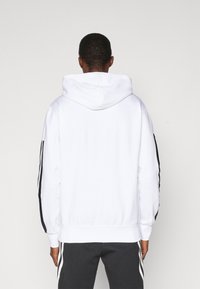 Sudadera blanca con capucha y franjas negras en los laterales, con mangas largas, puños y dobladillo de canalé, hecha de una suave mezcla de algodón.