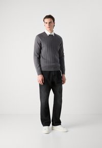 Grau gerippter Pullover mit Rundhalsausschnitt, kombiniert mit dunklen Jeans und weißen Sneakers. Sauberes Design mit strukturiertem Finish und tailliertem Schnitt.