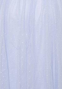 Ljusblått genomskinligt tyg med små vita broderade prickar och mjuka veck som skapar ett fint, texturerat mönster.