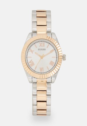 Round watch with silver and rose gold stainless steel band, white dial, Roman numerals, and textured bezel.  Brand name "Guess" displayed.