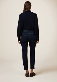 Un suéter de punto azul marino combinado con unos jeans de mezclilla azul oscuro. Los jeans tienen una cintura alta, bolsillos traseros y un diseño ajustado.