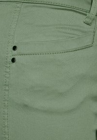 Tissu en coton vert des pantalons avec une poche latérale et des accents en métal noir. La texture semble lisse avec de fins détails de couture.