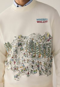 White sweatshirt with "WHERE'S WALLY?" text. Features colorful illustration of a snowy landscape filled with skiers and trees.