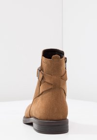 Brun mockaskinnsmidstövlett med en texturerad yta, med ett sidofäste och en robust brun träsula. Baksidan visas.