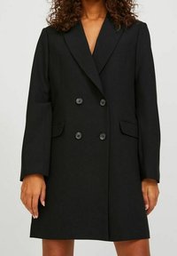 Svart dubbelknäppt blazer i slät väv, med slagkrage, två framfickor och stora svarta knappar. Avspänd passform.