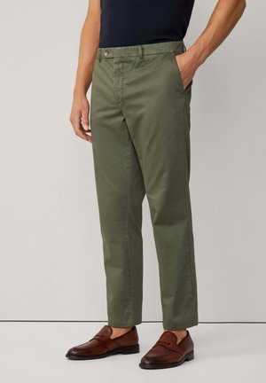 Olivgrüne Baumwoll-Chinos mit Seitentaschen, geradem Bein und Knopfverschluss, kombiniert mit braunen Loafers.