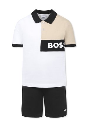 Camisa polo blanca con detalles en beige y negro, que presenta un logo negro de "BOSS". Combinada con pantalones cortos negros, ambos hechos de una tela suave.