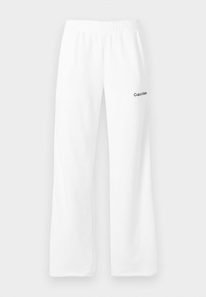 Bílé tepláky s elastickým pasem a logem Calvin Klein na horní levé stehně, zobrazené na neutrálním pozadí.