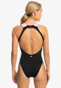 Black swimsuit with a racerback design, featuring pink shoulder straps and light green side panels. Notable back cutout and logo detail.