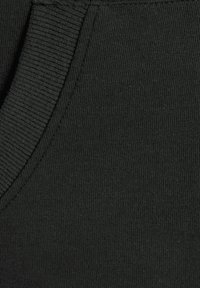 Gros plan sur un tissu noir d'un vêtement présentant des bords côtelés et une texture lisse, mettant en valeur une couture latérale et des détails de poche.