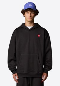 Musta huppari etutaskulla, jossa on pieni punainen logo. Yhdistettynä siniseen lippikseen. Yksinkertainen, rento muotoilu; sileä pinta.