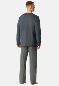 Herren-Loungewear-Set mit einem grauen Langarmoberteil und gemusterten grauen Schlafanzughosen mit lockerer Passform und weichem Stoff.