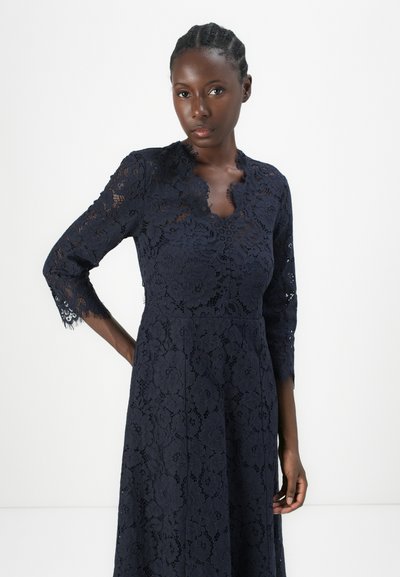 Navy blue lace dress with three-quarter sleeves, floral pattern, scalloped neckline, and textured fabric. Fitted bodice leading to a flared skirt.