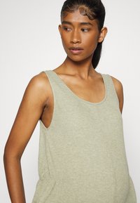 Top de alças em verde claro com decote redondo e alças largas, apresentando detalhes franzidos na cintura.