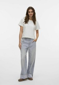 Chemise blanche à manches courtes avec une coupe large, associée à un jean large bleu clair avec des ourlets effilochés et des chaussures brunes décontractées.