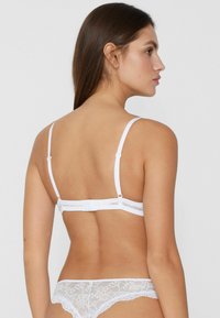 White lace bra with adjustable straps, featuring a hook-and-eye closure and floral pattern on the band, textured fabric.