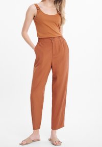 Hnědé tílko s ozdobnými ramínky, spojené s volnými kalhotami s vysokým pasem ve stejné hnědé barvě, doplněné béžovými nazouvacími botami.