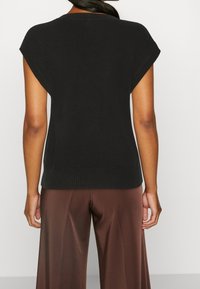 Maglione nero a maniche corte con orlo a coste e texture morbida, abbinato a pantaloni larghi marroni. La parte posteriore presenta un design semplice e pulito.