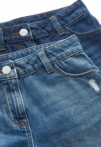 Se exhiben dos pares de jeans de mezclilla azul. Un par es más claro, con efecto de desgaste y detalles de desgarro, mientras que el otro es de un tono más oscuro.