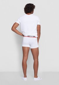 White cotton boxers with a red and black elastic waistband featuring the brand name. Model wearing a plain white t-shirt and white socks.