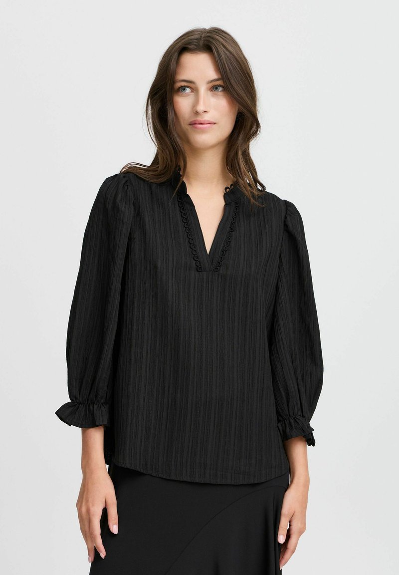 Blouse rayée noire avec un décolleté en V, accentuée par des manches volantes et un tissu texturé. Design simple et coupe régulière.