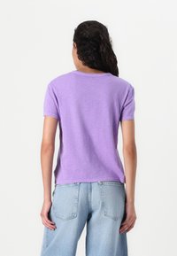 Tettsiddet lilla bomulls t-skjorte med korte ermer, rund hals og en teksturert overflate. Kombinert med lyseblå denimjeans.