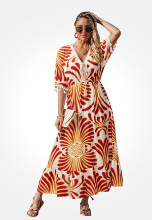 Mujer que lleva un vestido maxi blanco con estampados florales rojos y amarillos, gafas de sol, pendientes de aro, sostiene un bolso de mano tejido y sandalias.