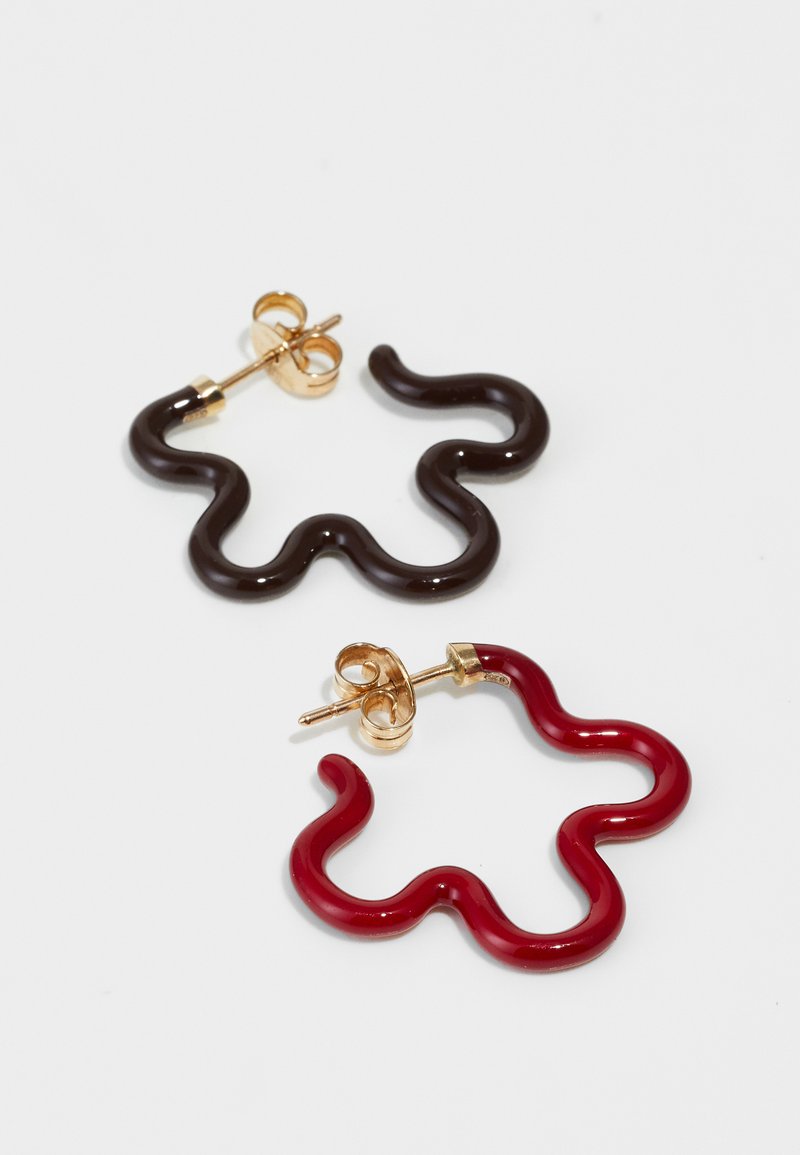 Um par de brincos em argola com formas onduladas; um em plástico preto brilhante, o outro em plástico vermelho, ambos com ferragens em metal dourado.