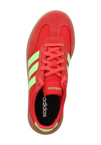 Sneaker rossa con tomaia in suede e materiale sintetico, presenta tre strisce verde neon, punta rotonda e suola in gomma. Marchio sulla linguetta e sulla soletta.