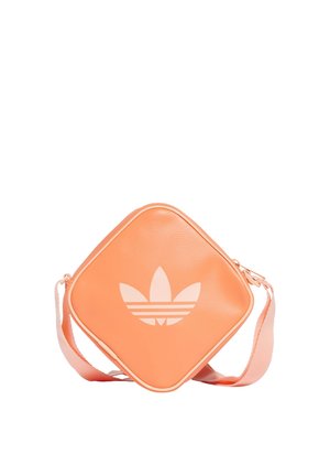 Kwadratowa torba na ramię w kolorze brzoskwiniowym z dużym białym logo Adidas w kształcie koniczyny i regulowanym paskiem na białym tle.