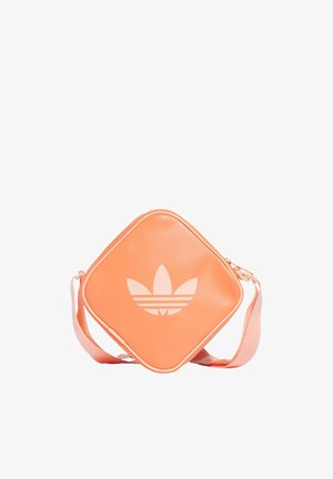 Vierkante schoudertas in perzikkleur met een groot wit Adidas trefoil-logo en verstelbare band op een witte achtergrond.