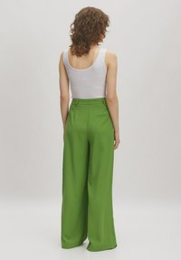 Green wide-leg trousers with a smooth texture, high waist, and back pocket detail. Paired with a white tank top.